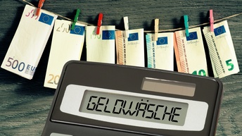 An einer Wäscheleine sind sieben unterschiedliche Eurogeldscheine mit Wäscheklammern fixiert. Davor ist ein Taschenrechner, auf dem Geldwäsche steht.