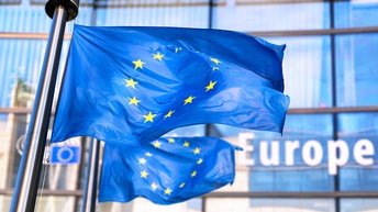 Zwei EU-Flaggen im Wind wehend, im Hintergrund Hausfassade mit dem Schriftzug Europe