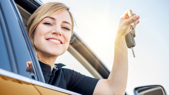 Lächelnde Person aus Autofenster gebeugt hält Autoschlüssel in die Luft