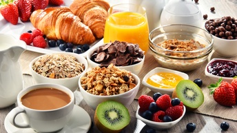 Reichhaltiger Frühstückstisch mit Kaffee, Orangensaft, Obst, Zerealien sowie Croissants