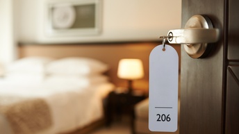 Detailansicht Türklinke mit Schlüssel samt Anhänger mit Aufschrift 126, im Hintergrund verschwommen Hotelzimmer