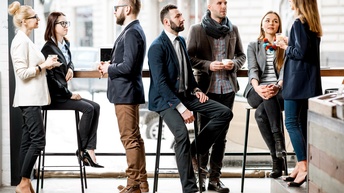 Gruppe von Personen in Businesskleidung steht und sitzt in einer hellen und modernen Cafeteria und unterhält sich