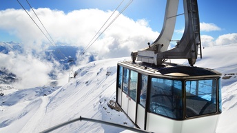 Eine weiße Gondel an Stahlseilen hängend in verschneiter Berglandschaft