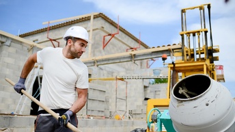 Person mit Schutzkleidung arbeitet bei Mischmaschine am Bau und fertigt einen Ziegelbau