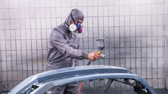 Karosserielackierer mit Schutzmaske und Sprühpistole lakiert eine Karosserie