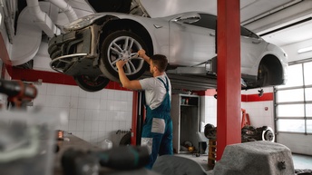 Person schraubt an Reifen eines Autos, das sich auf Hebetribüne befindet