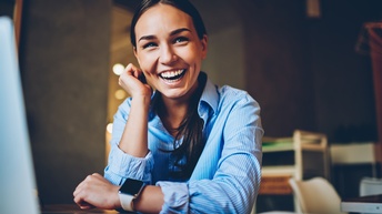 Lachende Person in blaugestreiftem Hemd stützt einen Arm an die Wange, der andere Arm am Tisch abgestützt mit iWatch am Handgelenk
