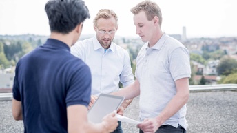 Drei Personen stehen um einen Installationsplan zusammen