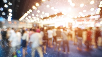 Verschwommene Aufnahme mehrerer Personen in einem Raum, die stehen oder sich bewegen. Darüber liegt eine Grafik, bestehend aus feinen, weißen Strichen, die kreuz und quer über das Bild verlaufen und miteinander verbunden sind