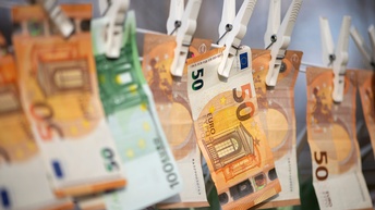 Nahaufnahme einer Wäscheleine, an der viele Geldscheine mit Wäscheklammern befestigt sind. Auf manchen Geldscheinen steht 100, auf anderen 50.