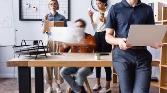 Mitarbeitende arbeiten hastig mit unterschiedlichen Unterlagen und Materialien bei einem Schreibtisch, Startup