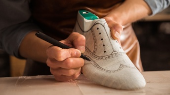 Ein Schuhmacher erstellt einen Prototypen eines Herrenschuhes und zeichnet das Muster auf den Schuh.