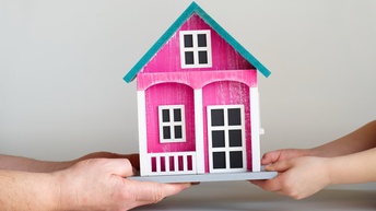 Eine erwachsene Hand und eine Kinderhand halten beide gemeinsam ein Miniatur-Haus