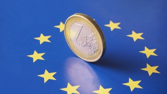 Auf einer Flagge der europäischen Union in der Mitte im Sternenkreis steht eine ein Euromünze