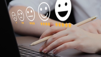 Nahaufnahmen einer Hand, die Tastatur eines Laptops mit den Fingerspitzen berührt und einen Bleistift hält. Darüber sind fünf Emojis als Grafik gelegt. Unter jedem Emoji sind Sterne. Ganz links einer, dann zwei, dann drei, dann vier, dann fünf