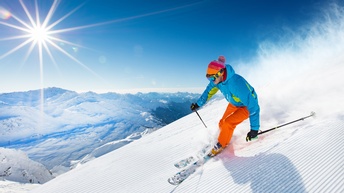 Schifahrende Person, im Hintergrund verschneite Gebirgslandschaft, Sonne und blauer Himmel