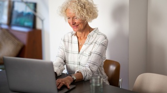 Lächelnde Person sitzt an Tisch und blickt auf Laptop