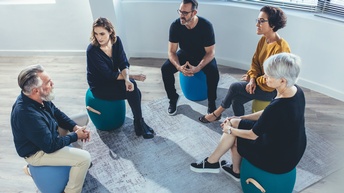 Mehrere Personen sitzen im Kreis auf blauen Hockern und unterhalten sich