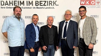 Fünf Männer stehen nebeneinander vor einem Hintergrund mit dem Logo der Wirtschaftskammer Tirol (Bezirksstelle Landeck). Sie tragen überwiegend Business- oder Smart-Casual-Kleidung: Hemden, Jacketts, Jeans oder Stoffhosen. Alle blicken in die Kamera und lächeln leicht. Die Szene wirkt wie ein offizieller Fototermin im Rahmen einer Veranstaltung oder eines Servicetags.
