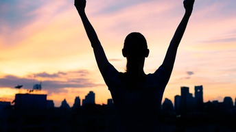 Frau in Siegerpose bei Sonnenaufgang mit Skyline Stadt