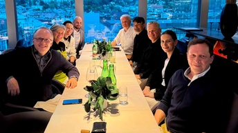 Mehrere Menschen sitzen an einem Tisch und lächeln in die Kamera