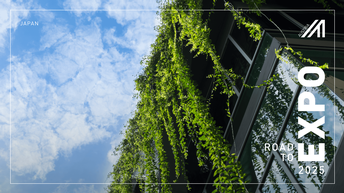 Blick von unten auf eine begrünte Fassade eines modernen Gebäudes mit Glasfront vor einem blauen Himmel mit weißen Wolken