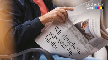 Eine Person sitz und hält eine aufgeschlagene Zeitung