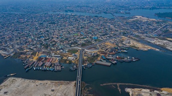 Top- Shot der Stadt Port Harcourt in Nigeria, die an einem Gewässer liegt mit vielen unterschiedlichen Gebäuden sowie Straßen, die durch die Stadt führen. Im Gewässer sind Anlegestellen für Boote und Frachtschiffe. Über das Gewässer führen Brücken