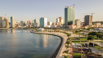 Stadtansicht von Luanda, am Wasser gelegen: Blick auf die mit Palem bewachsene Promenade in der Luanda Bay. Im Hintergrund ragen Wolkenkratzer in die Höhe.