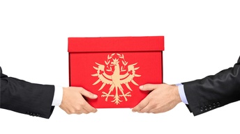 Zwei Hände halten ein rotes Paket, auf dem in der Tiroler Adler in goldener Farbe abgebildet ist