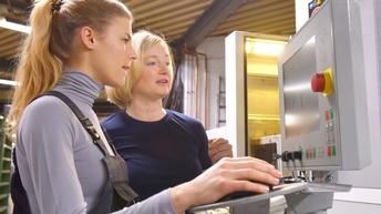 Zwei Personen stehen vor Monitor einer Anlagenregelung, eine Person hält Steuerungsmaus in Hand