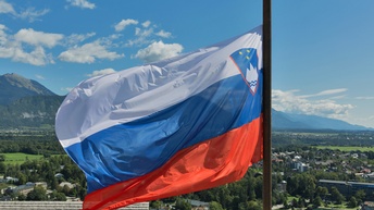 Die slowenische Flagge weht im Wind, im Hintergrund eine Stadtansicht.
