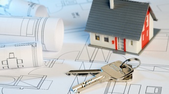 Nahaufnahme eines Plans von Wohnräumen, auf dem Papierrollen, ein Schlüssel und ein kleines Modell eines Hauses sind.