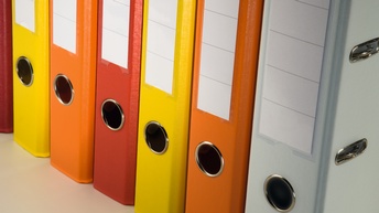 Mehrere rote, gelbe, weiße und orange Aktenordner aneinander gereiht