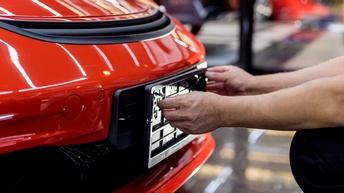 Hände befestigen ein Nummernschild an einem roten Auto