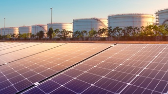 Solarpanele im Vordergrund, im Hintergrund Ölspeicher im Sonnenuntergang