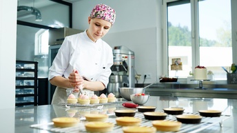 Eine junge Konditorin dekoriert Törtchen mit einem Spritzbeutel
