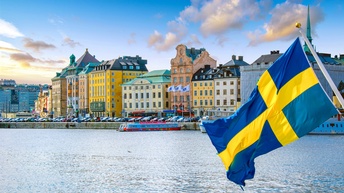 Die schwedische Flagge weht im Wind, im Hintergrund eine Stadtansicht.