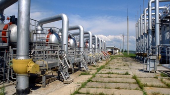 Metallische Gastanks mit Röhren gegenüberliegend , in der Mitte betonierter, von Pflanzen durchbrochener Weg unter blauem Himmel mit Wolken