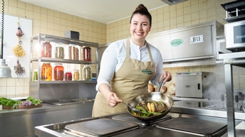 Lächelnde Person mit Schürze in Küche stehend hält Pfanne in der Spargel gebraten wird