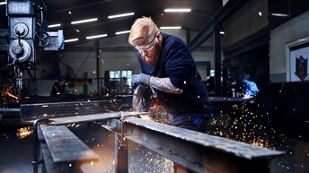 Ein Mann sägt an einem Metallteil, das auf zwei Metallträger gespannt ist