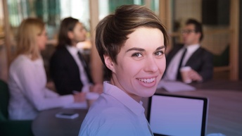 junge Frau im Vordergrund lächelt in die Kamera. Im Hintergrund zwei Frauen und ein Mann