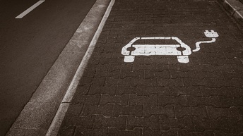 Auf einem Parkplatz, der neben einer asphaltierten Straße ist, ist ein Symbol eines Autos mit einem Stecker aufgemalt