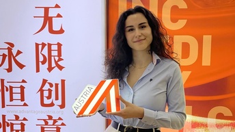 Eine junge Frau hält eine Austria-A-Zeichen in der Hand. Im Hintergrund chinesische Schriftzeichen