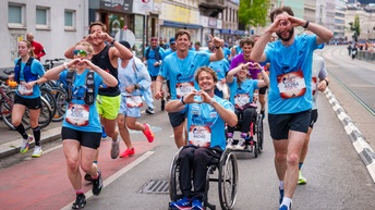 Personen in blauen T-Shirts laufen und schieben mehrere Rollstuhlfahrer