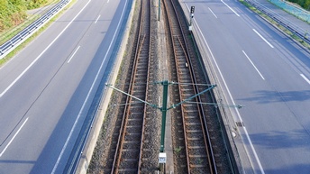In der Mitte sind zwei Gleise parallel nebeneinander. Links und rechts von den Gleisen ist jeweils eine mehrspurige Straße