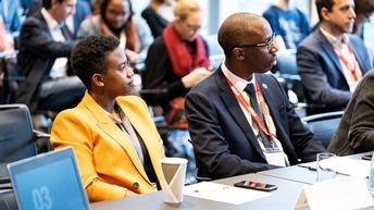 Gemischtes vor einem Tisch sitzendes Publikum bei einem Vortrag<br />
