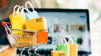 Miniatur-Einkaufswagerl mit Taschen und Paketen steht  auf Laptop.