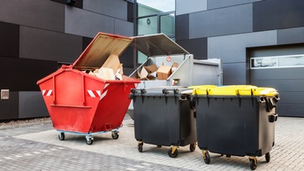 Verschiedene Abfallcontainer für Restmüll, Plastik und Kartongen vor schwarzer paneelierter Hausfassade