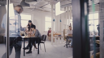 Personen arbeiten in einem Großraumbüro in unterschiedlichen Abschnitten des Raumes